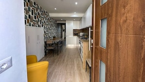 A modern kitchen with wooden cabinets, a dining area with a yellow chair, and a patterned wall.
