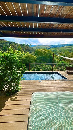 En træterrasse med en pool, omgivet af frodig vegetation og bakker i baggrunden.