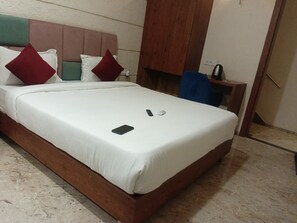 A neatly made bed with a white bedspread and pillows, a wooden headboard, and a small bedside table with a kettle.
