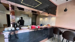 A modern kitchen with a black marble countertop, a person cooking, and a bar area with stools. - Acuotel Inn Minakshi (Indore)