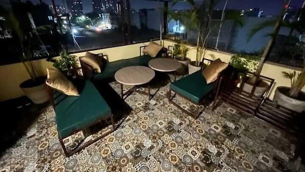 A rooftop terrace with a patterned floor, green cushioned seating, and potted plants. - Acuotel Inn Minakshi (Indore)