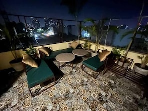 Terraza en la azotea con piso estampado, asientos acolchados verdes y plantas en macetas.