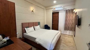 A hotel room with a bed, a desk, a chair, a ceiling fan, and a TV mounted on the wall. - Acuotel Inn Minakshi (Indore)
