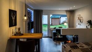 A modern living room with a wooden dining table, a sofa, a TV, and a view of a garden through a glass door. - Apartment 'Mellies' with Private Terrace, Garden and Wi-Fi (Willingen (Upland))