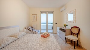 Et soveværelse med seng, stol, skrivebord, et vindue og en dør der fører ud til en balkon.
