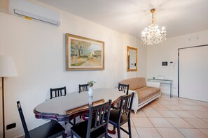 A dining area with a table, chairs, a chandelier, a painting, and a sofa.