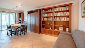 Ein großzügiger Wohnbereich mit Esstisch, Stühlen, einer Couch und einem großen Bücherregal, gefüllt mit Büchern.