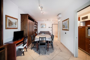 A room with a dining table, chairs, a television, a bookshelf, and framed pictures on the walls.