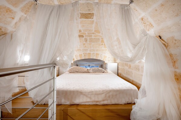 A bedroom with a bed, a wooden floor, a stone wall, and a metal railing.