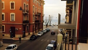 Straßenansicht mit parkenden Autos, einem Fußgänger und Gebäuden mit Balkonen.
