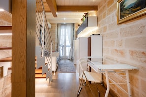 A modern interior with a wooden staircase, a white desk, and a view through a window with curtains.