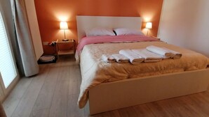 Un lit bien fait, avec une couvre-lit et des oreillers de couleur beige, une table de chevet avec une lampe et un plancher en bois.