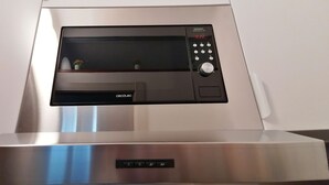 Un four à micro-ondes moderne doté d’un écran numérique et d’un panneau de commande, fixé sur une hotte de cuisine en acier inoxydable.