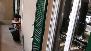 Un couloir doté d’un sol carrelé, de volets verts et d’une porte donnant sur une pièce avec une grande fenêtre.