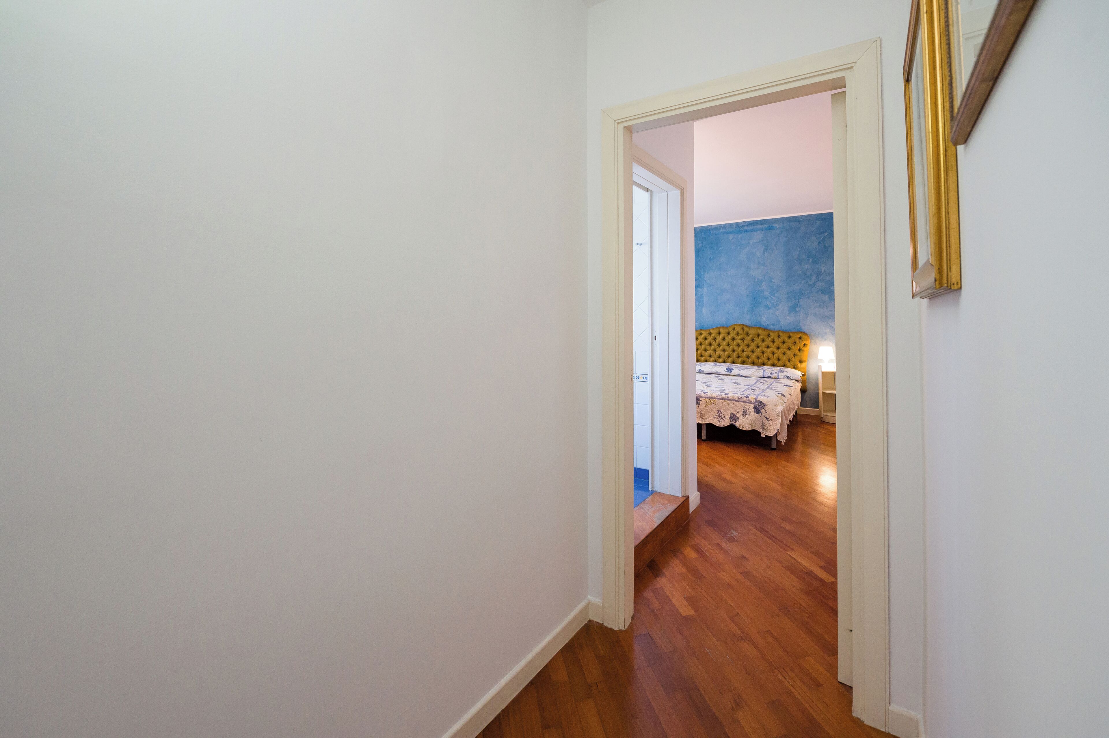 A hallway leading to a bedroom with a bed, a nightstand, and a blue wall.