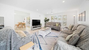 Ein modernes Wohnzimmer mit einer Couch, einem Couchtisch, einem Fernseher und einem Essbereich mit Stühlen und einem Tisch.