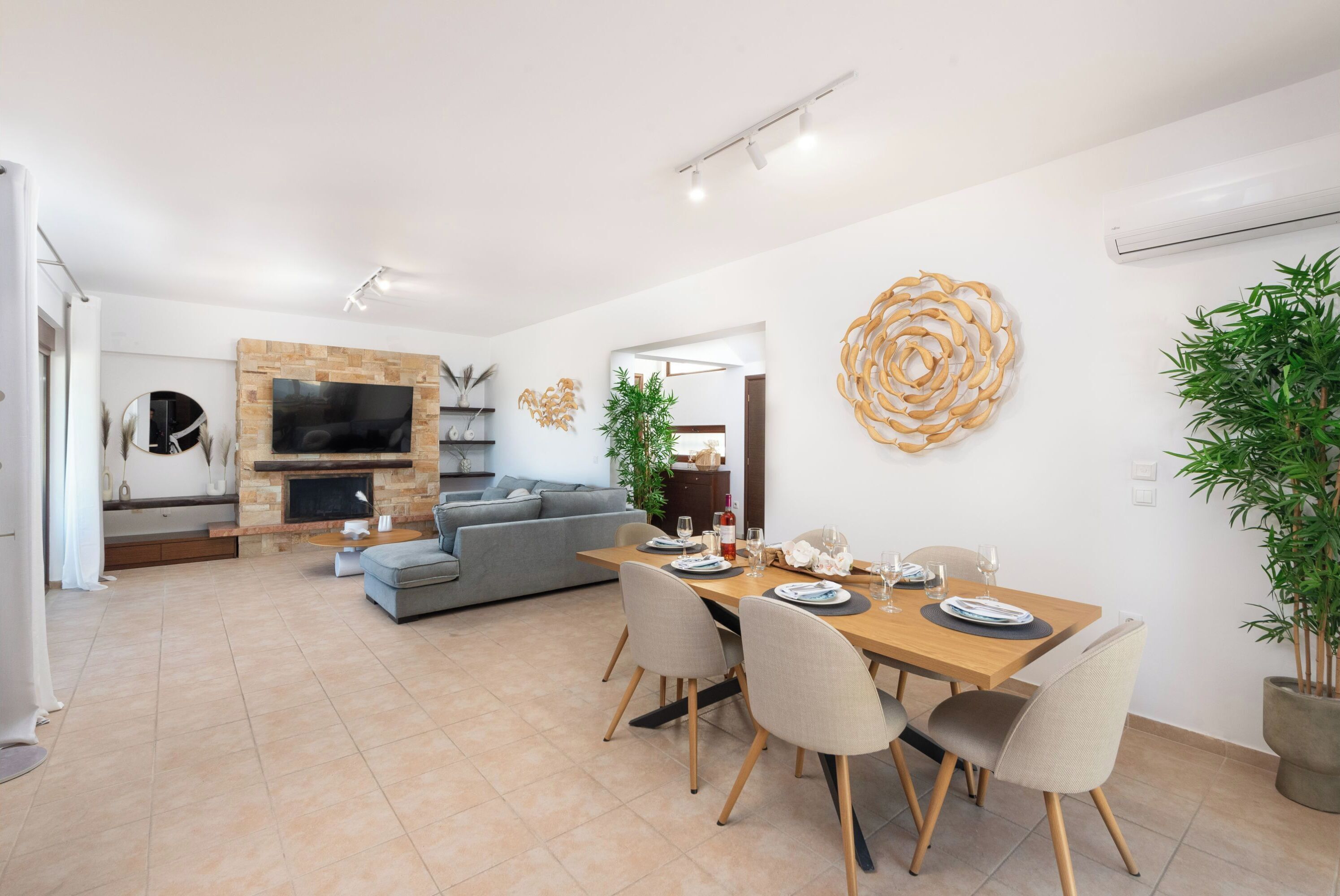 A modern living room with a fireplace, a dining area with a wooden table and chairs, and a grey sofa.