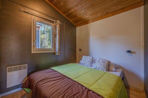 A bedroom with a bed, a window with curtains, a radiator, and a wooden ceiling. - Chalet 'Montana 5_4 Pers' with Mountain View, Shared Pool and Wi-Fi (Roquefeuil)