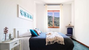 A bedroom with a bed, a nightstand, a window with a view, and a chair.