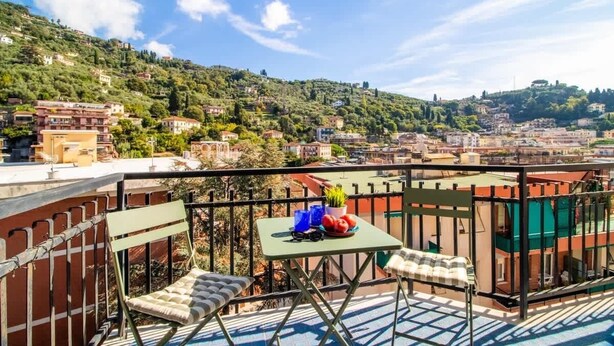 A balcony with a table, chairs, and a view of a hillside town.