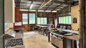 A rustic kitchen with a gas stove, wooden cabinets, and a large window overlooking greenery. - Christmas Creek Rainforest Retreat, ultimate nature filled group getaway. (Lamington)