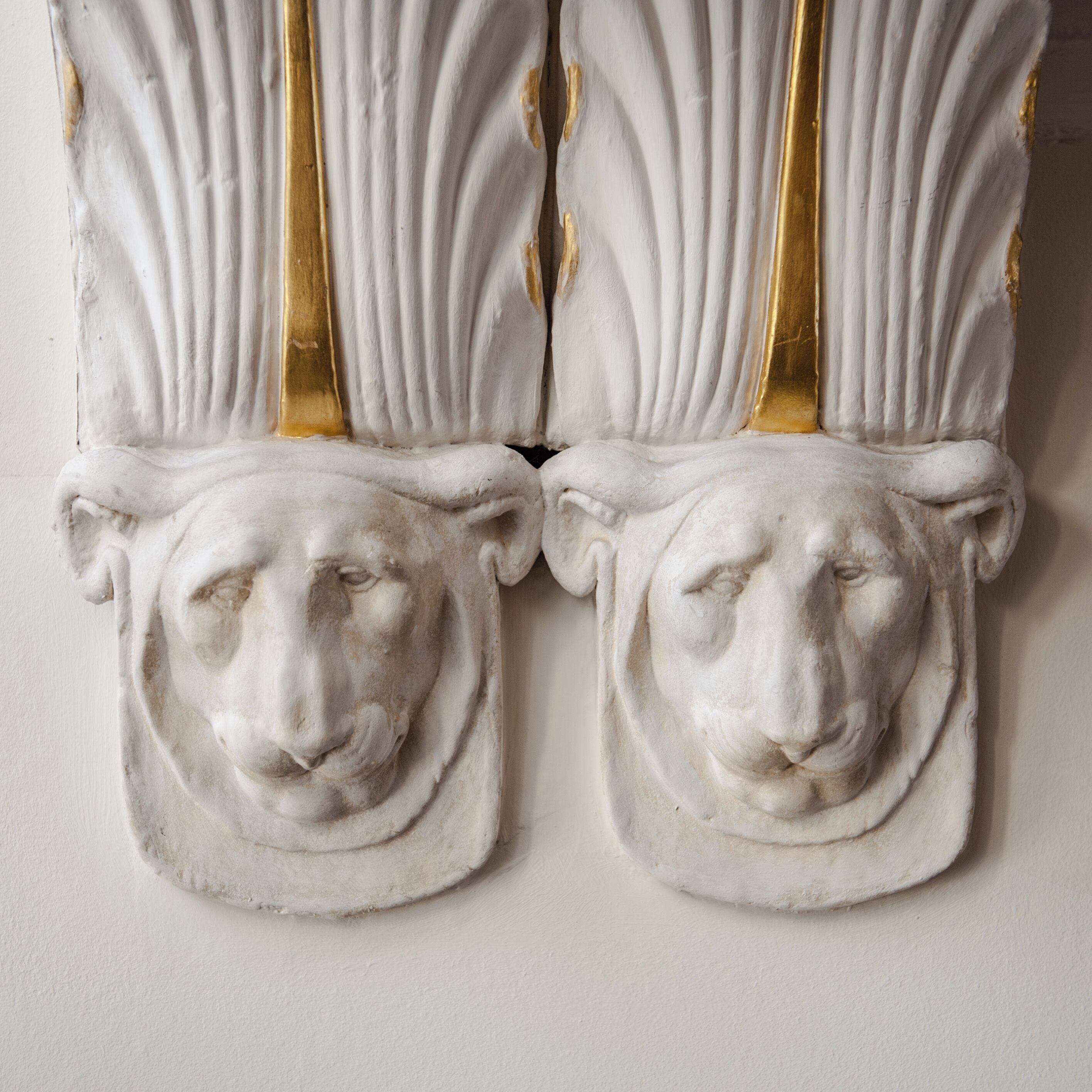 A white wall with two white, gold-framed decorative panels featuring a classical design.