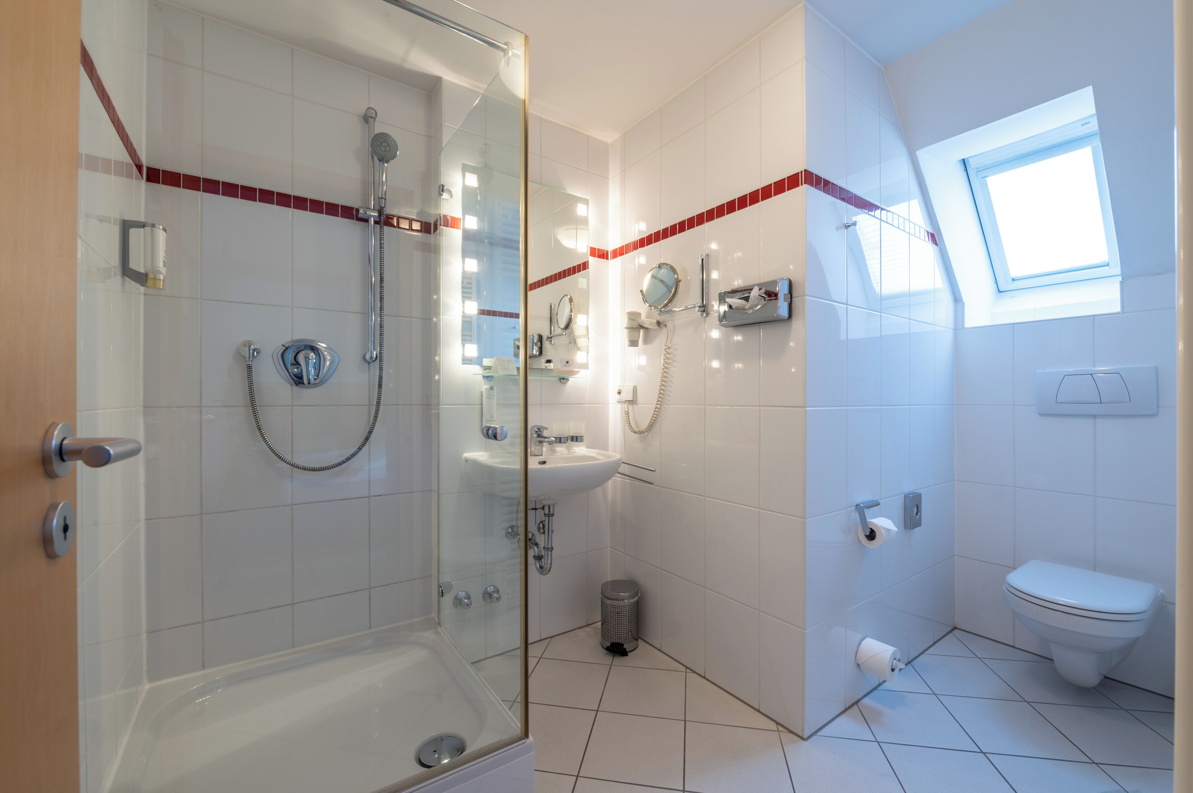 A modern bathroom with a glass-enclosed shower, a sink, a toilet, and a small trash bin.