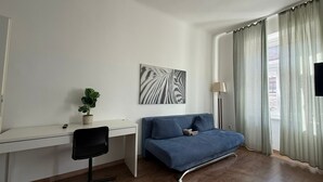A modern bedroom with a blue sofa, a desk with a chair, a potted plant, and a zebra-striped artwork. - 1BR Apt Budget Stay by Westbahnhof (Vienna)