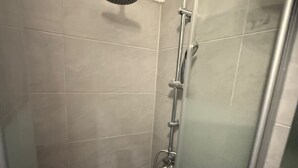 A shower area with a handheld showerhead, a vertical rain showerhead, and a glass-enclosed shower stall. - 1BR Apt Budget Stay by Westbahnhof (Vienna)
