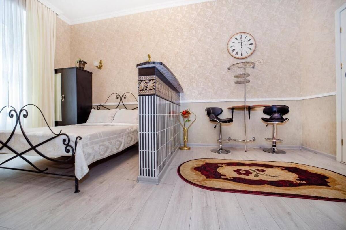 A bedroom with a bed, a desk, two chairs, a clock, and a radiator.