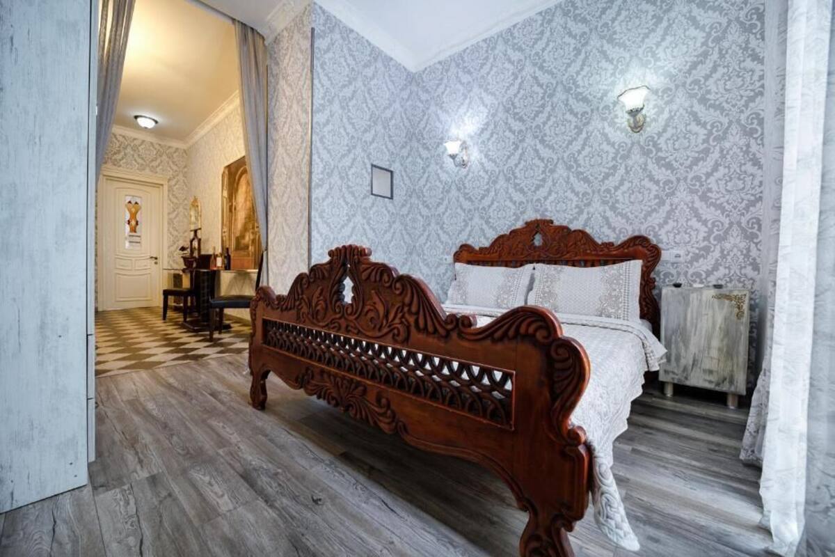 A bedroom with a wooden bed, patterned wallpaper, and a checkered floor.