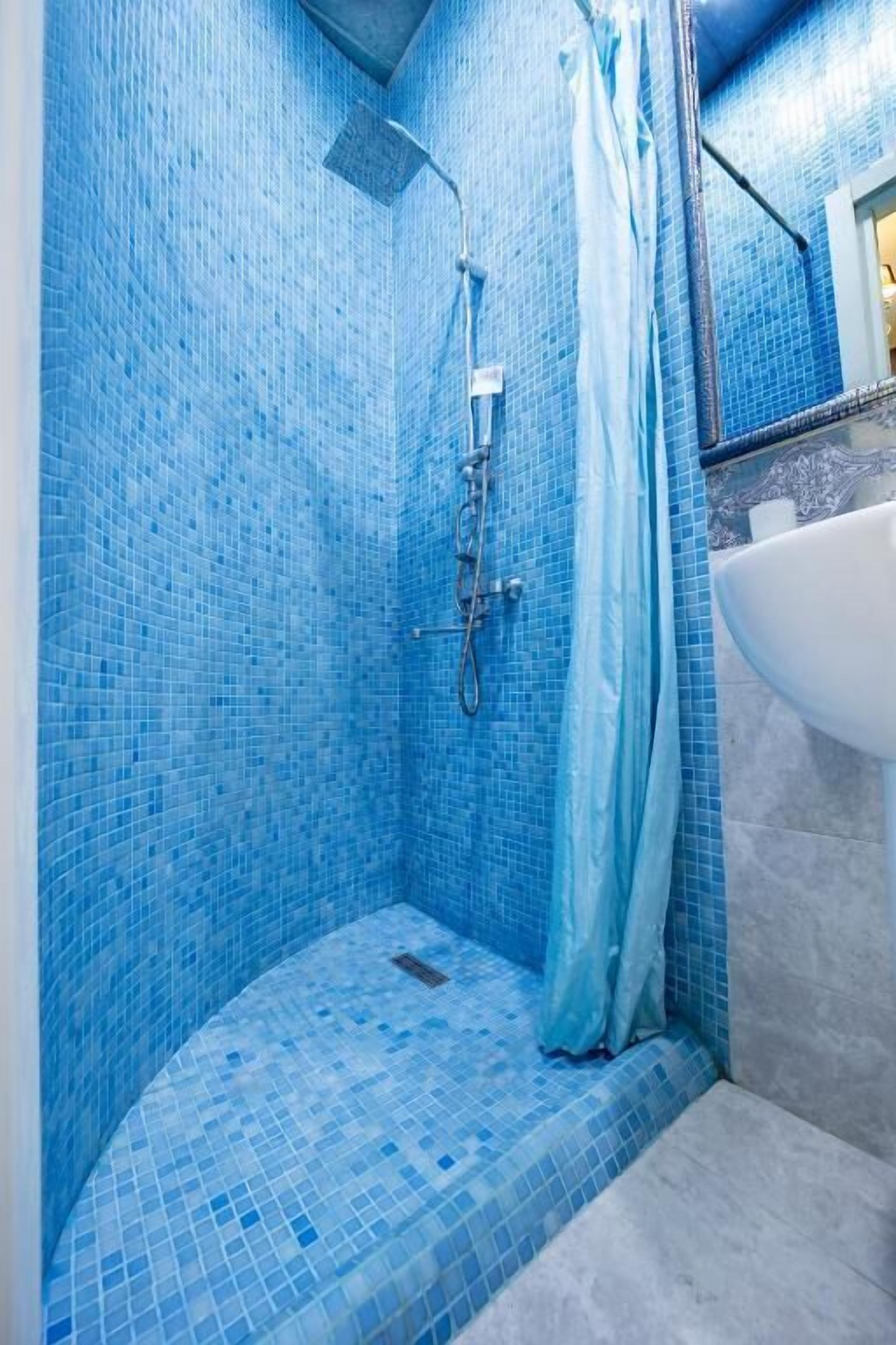 A bathroom with blue mosaic tiles, a shower, and a sink.