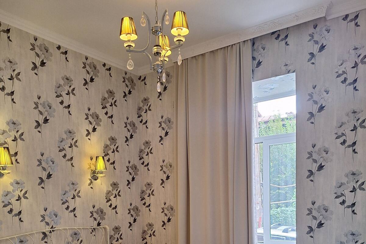 A bedroom with a bed, a chandelier, a window with curtains, and a radiator.