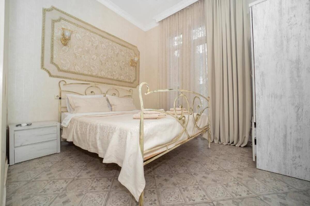 A neatly arranged bedroom with a bed, a nightstand, and a large window with curtains.