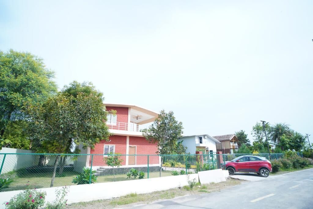 Una casa de dos pisos con fachada roja, un patio cercado y un coche rojo estacionado al frente.