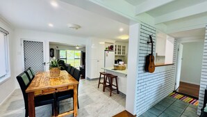 A modern kitchen with white cabinets, a wooden dining table, and a guitar wall decoration. - "Bills Place" @ Brunswick - House - Sleeps 8 - Walk to Beach, Creek & Main Town (Brunswick Heads)