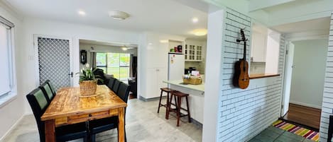 Een moderne keuken met witte kastjes, een houten eettafel en een gitaar aan de muur.