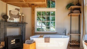 Une salle de bain moderne avec une baignoire sur pieds, un poêle à bois et une grande fenêtre donnant sur la forêt.