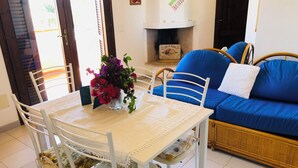 A dining area with a white table, chairs, and a vase of flowers. There is a blue sofa and a fireplace in the background. - Three-room apartment Oleander 300 mt beach San Teodoro (San Teodoro)