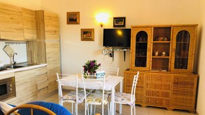 A compact kitchen with a dining area, wooden cabinets, a TV, and a small cabinet with glass doors. - Three-room apartment Oleander 300 mt beach San Teodoro (San Teodoro)