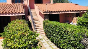 A pink villa with a tiled roof, a staircase leading to a covered porch, and a well-maintained garden. - Three-room apartment Oleander 300 mt beach San Teodoro (San Teodoro)