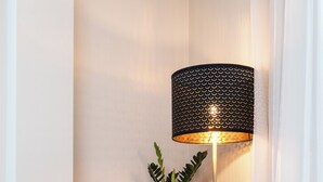 Ein modernes Schlafzimmer mit einem grauen Sofa, einer Stehlampe und einer Pflanze.
