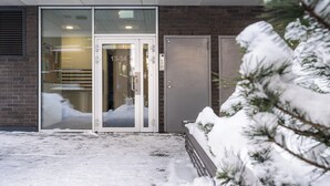 Ein Gebäudeeingang mit Glastür, Ziegelwand und verschneitem Boden.