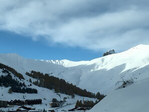 Ein mit Schnee bedeckter Berg unter blauem Himmel. Am Fuße des Berges befinden sich Gebäude, vermutlich ein Resort oder eine Berghütte.