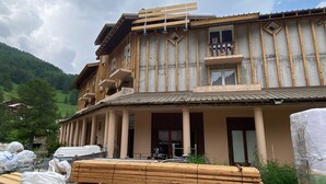Un edificio de varios pisos con balcones, amplias ventanas y un paisaje montañoso al fondo.