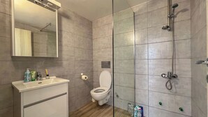 Un baño moderno con ducha de vidrio, lavamanos blanco y retrete.