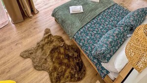 Un dormitorio acogedor con una ventana grande, una cama con ropa de cama floral, un tapete de piel sintética y una cesta tejida.