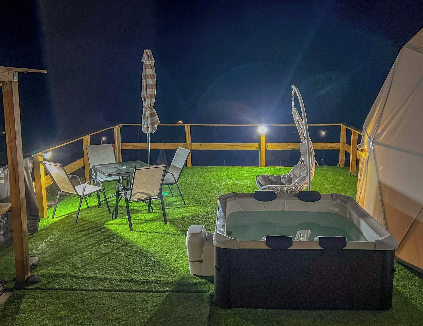 Un espace extérieur aménagé avec une tente, un jacuzzi, des chaises et un parasol.