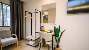 Een moderne kamer met een bank, een bureau met stoel, een kledingrek, een grote spiegel, een televisie en een kamerplant.