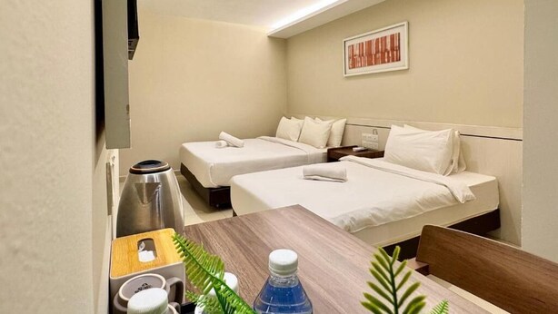 Een hotelkamer met twee bedden, een houten tafel, een waterkoker, een fles en een lijst met kunst.